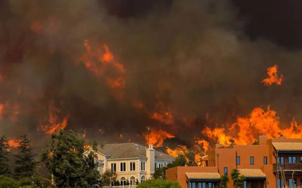 Homes with a wall of wildfire burning directly behind them